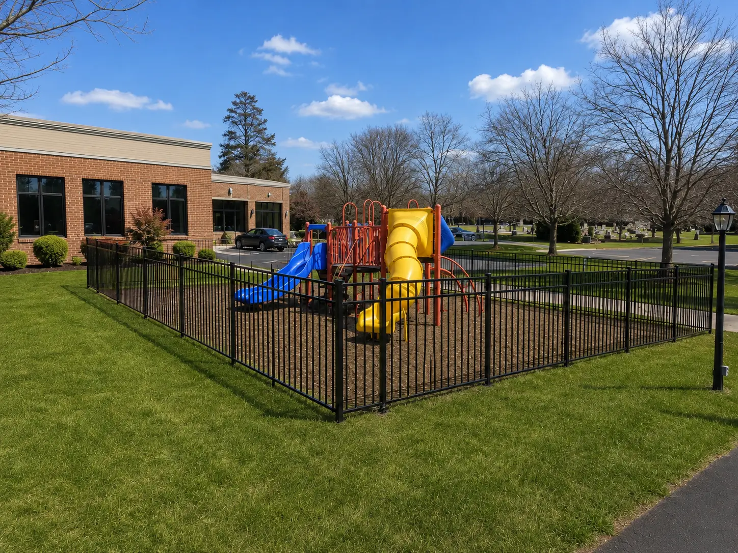 Black aluminum fence enclosing a commercial playground with brick building in New Jersey installed by Fred's Fence