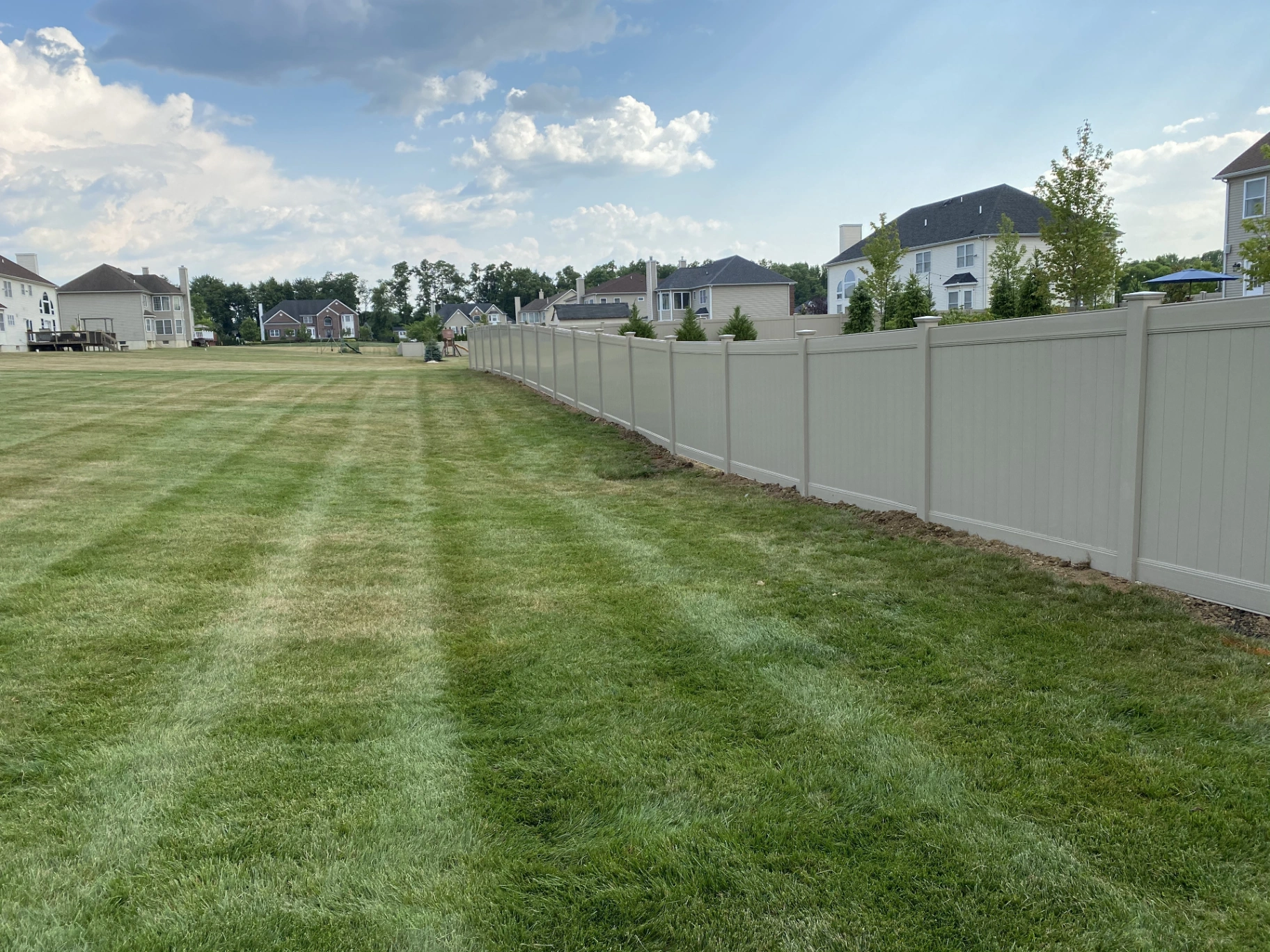 Tan vinyl privacy fence with decorative top accent installed along a residential property in New Jersey by Fred's Fence