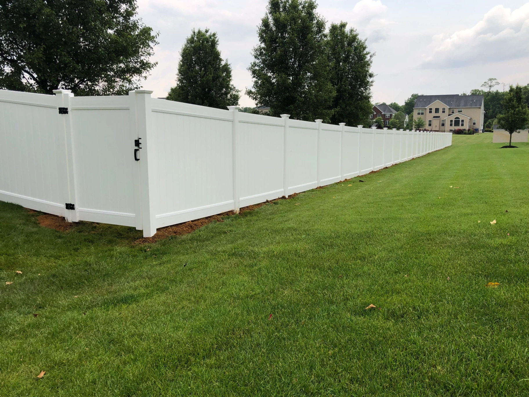 White vinyl privacy fence with gate along a residential property line in New Jersey by Fred's Fence